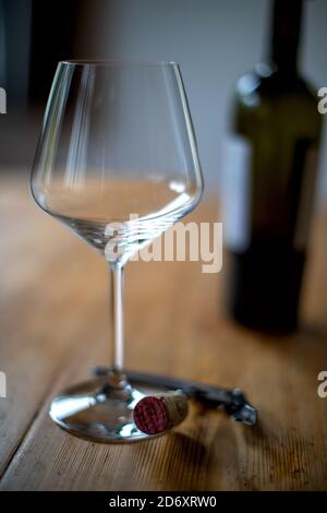 empty red wine glass wit corkscrew on a wooden old table, in the back a bootle Stock Photo