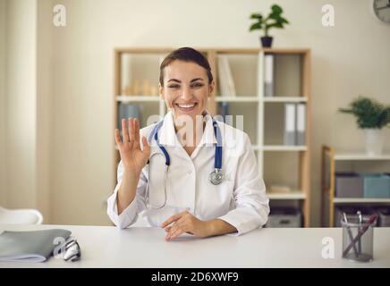 Young smiling doctor therapist looking at camera and greeting somebody online Stock Photo