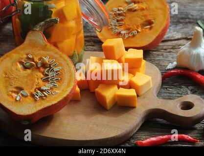 Chopped pumpkin on rustic cutting board and ingredients for tasty vegetarian cooking, dark styled . Stock Photo