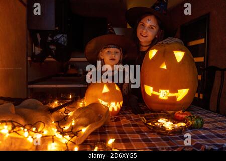 Woman and child girl having fun and celebrate Halloween in witch costume. Mother and daughter makes pumpkins jack-o-lantern. Stock Photo