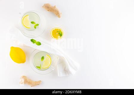 Ginger tea with lemon and mint on a white napkin. Two cups of ginger tea, lemon, ginger root and honey on white background. Top view Stock Photo