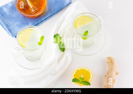 Ginger tea with lemon and mint on a white napkin. Two cups of ginger tea, lemon, ginger root and honey on white background. Top view Stock Photo