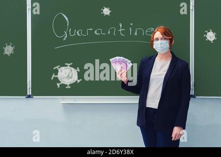 Woman teacher in a medical mask holds money in euros at the blackboard with the words Quarantine. Concept of money problems during isolation due to fl Stock Photo