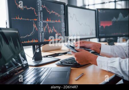 Close up view of woman's hands that holds money near the monitors with graphs Stock Photo