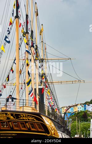 SS Great Britain stern view. Actor in dress uniform leaning on railing. Signal flags, dress ship rigging. Bristol Dockyard. GB. Colorful buildings. Stock Photo