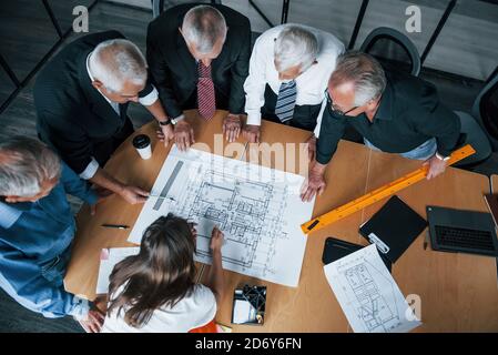 Top view of aged team of elderly businessman architects have a meeting in the office with young woman and works with plan Stock Photo