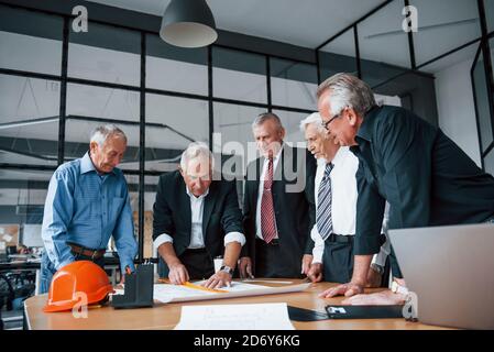 Aged team of elderly businessman architects works with plan in the office Stock Photo