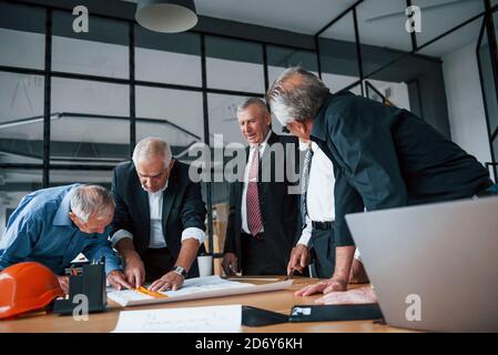 Aged team of elderly businessman architects works with plan in the office Stock Photo