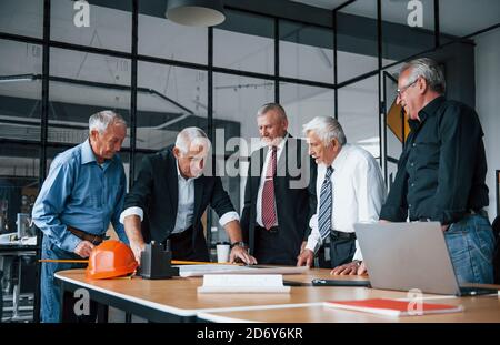Aged team of elderly businessman architects works with plan in the office Stock Photo