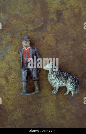 Battered vintage lead models of farmer with missing arm standing next to black and white sheepdog Stock Photo