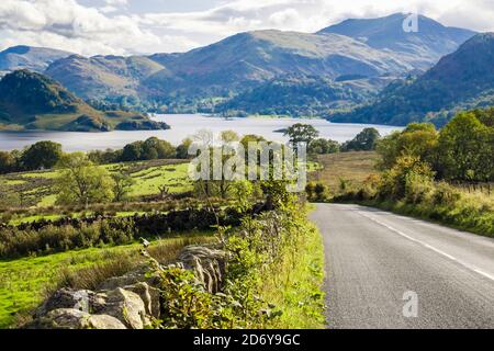 Stone wall and grass verge by A5091 country road with view down to Ullswater in Lake District National Park. Dockray, Cumbria, England, UK, Britain Stock Photo