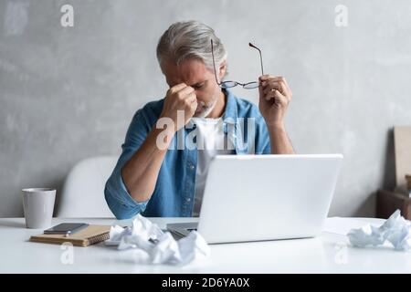 Stressed tired freelancer is having headache and thinking how to finish his work, holding the nose bridge, massaging it Stock Photo