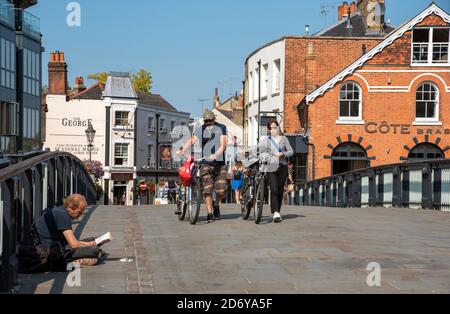 Eton, Buckinghamshire, England, UK. 2020. Cyclists push their bicycles past a man begging over the Windsor Eton bridge which crosses the River Thames Stock Photo