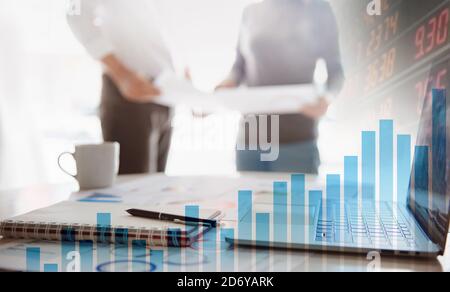 Two business people working together on corporate strategy. Try to analyze statistics. Financial forecast graph hologram. Double exposure. Stock Photo