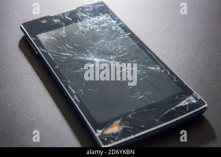 Smartphone with a broken cracked display on a dark background close-up Stock Photo