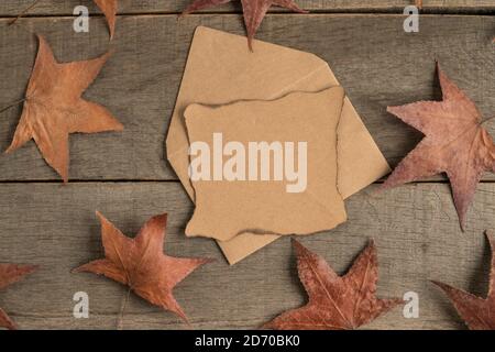 an empty paper and envelope on wooden table decorated with dried autumn leaves Stock Photo
