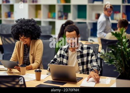 Two young diverse business colleagues using modern technologies while sitting at the desk and working together in coworking space. Office life, teamwork and business Stock Photo