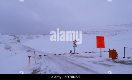 Skarsvåg, Norway - 02/28/2019: Closed gate at road to popular Nordkapp (North Cape) in winter with orange sign informing about the convoy hours. Stock Photo