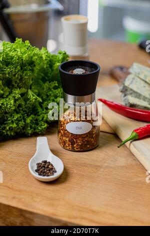 Chili in a glass container and peppercorns on a wooden table Stock Photo