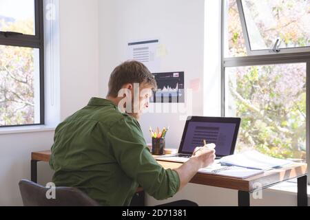 Caucasian man spending time at home, working from home, using laptop computer, making notes. Social distancing during Covid 19 Coronavirus quarantine Stock Photo