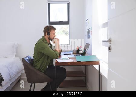 Caucasian man spending time at home, working from home, using laptop computer wearing phone headset. Social distancing during Covid 19 Coronavirus qua Stock Photo