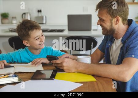 Caucasian man at home with his son together, in kitchen, father helping the boy doing homework at table. Social distancing during Covid 19 Coronavirus Stock Photo