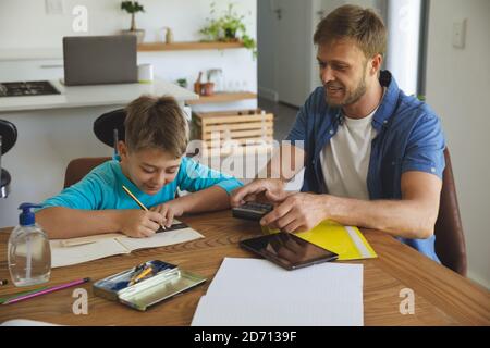 Caucasian man at home with his son together, in kitchen, father helping the boy doing homework at table. Social distancing during Covid 19 Coronavirus Stock Photo
