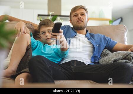 Caucasian man at home with his son together, sitting on sofa in living room, watching TV. Social distancing during Covid 19 Coronavirus quarantine loc Stock Photo