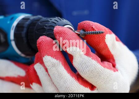 Electric screwdriver in the hands of a carpenter. Male hands in work gloves hold an electric screwdriver. Stock Photo