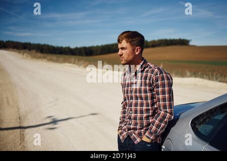 Man in casual clothes leaning on his car outdoors on the road. Rural scene Stock Photo