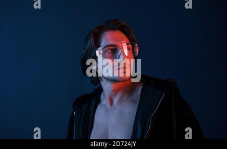 Beautiful long haired hot man in glasses is in the studio with blue neon lighting Stock Photo