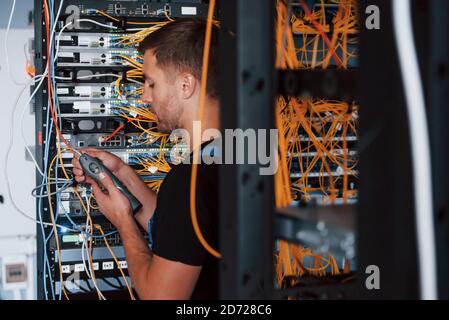 Young man in uniform works with internet equipment and wires in server room Stock Photo