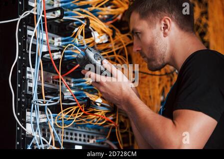 Young man in uniform works with internet equipment and wires in server room Stock Photo