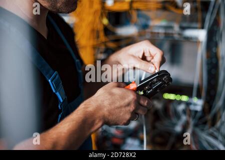 Young man in uniform works with internet equipment and wires in server room Stock Photo