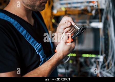 Young man in uniform works with internet equipment and wires in server room Stock Photo