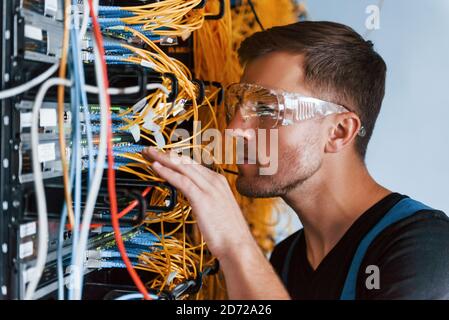 Young man in protective glasses works with internet equipment and wires in server room Stock Photo