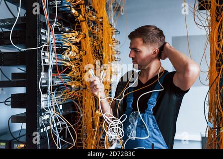 Young man in uniform feels confused and looking for a solution with internet equipment and wires in server room Stock Photo