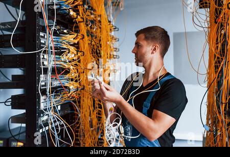 Young man in uniform feels confused and looking for a solution with internet equipment and wires in server room Stock Photo