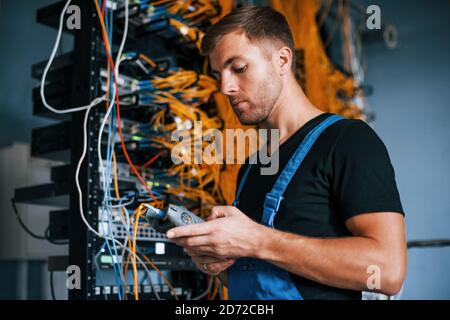 Young man in uniform have a job with internet equipment and wires in server room Stock Photo