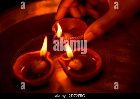 Indian woman or girl holding a lit clay diya in her hand and illuminating other oil lamps with it in a thali or plate. Hindu Festival Diwali rituals. Stock Photo