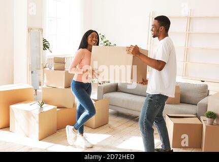 Full length of young black man with his girlfriend carrying cardboard box in their new home on moving day Stock Photo
