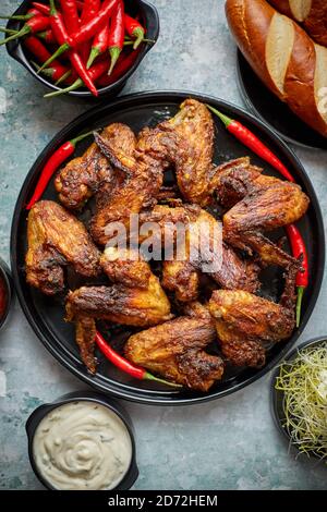 Grilled chicken wings with chilli pepper on a rustic plate served with various dips and bread Stock Photo