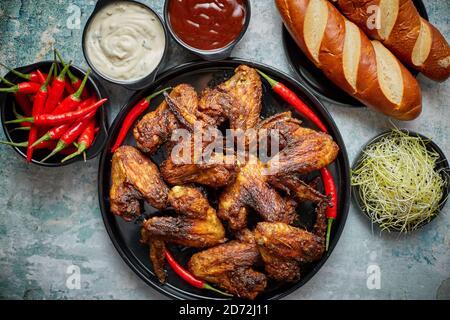 Grilled chicken wings with chilli pepper on a rustic plate served with various dips and bread Stock Photo