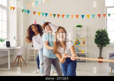 Group of happy multiracial children playing tug-of-war at birthday party at home Stock Photo