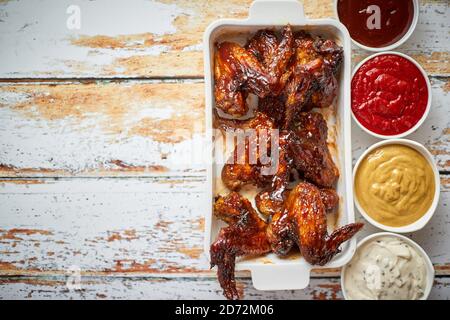 Chicken wings in thick barbecue sauce with various side dips. Served on white cast iron dish Stock Photo