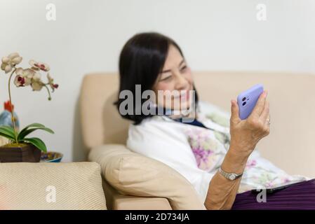 Selected focus happy senior woman sitting on couch using phone for video call. Stock Photo