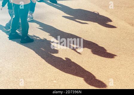 Children silhouettes and shadows on asphalt road, three children walking in a street Stock Photo