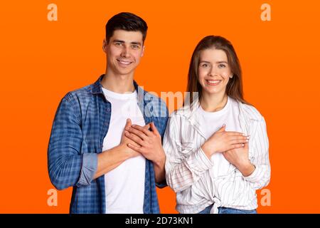 Grateful gesture concept. Pretty smiling young male and female in casual clothes keep hands on chest, being thankful Stock Photo