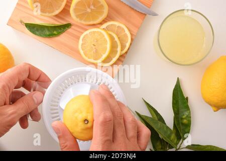 Hands squeezing a lemon in a plastic juicer with container for preparing a lemonade on the kitchen bench. Top view. Horizontal composition. Stock Photo