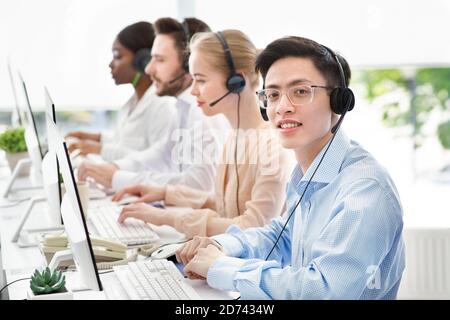 Asian call centre manager smiling and looking at camera in light office, space for text Stock Photo